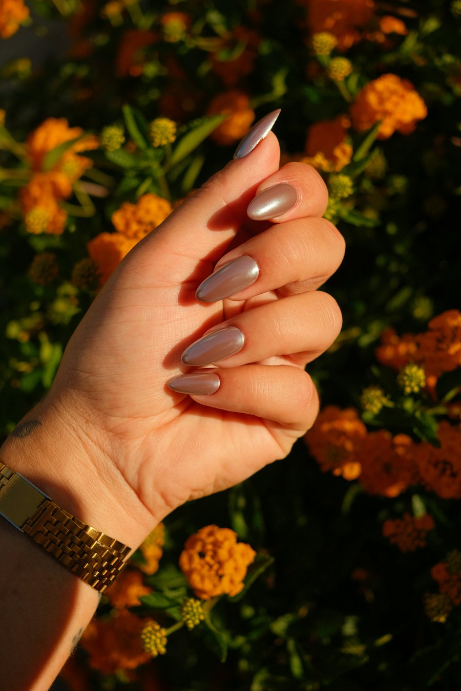 Hand with soft nude nails against orange flowers
