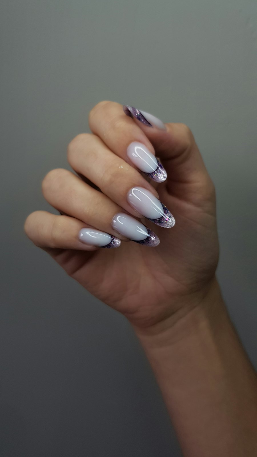 Hand with white and lilac marbled nails against a grey wall
