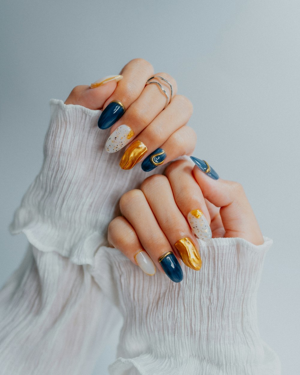 Hands with navy, gold and white nails in a ruffled sleeve