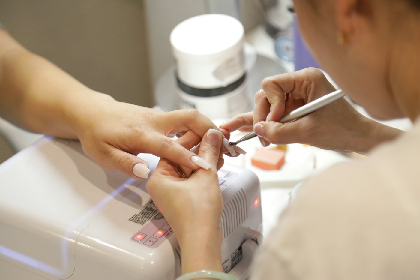 A nail technician filing a client's nails at a manicure station